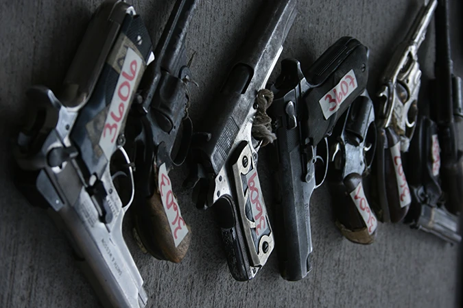 Several handguns, with numbers taped to their sides, laid out in a row. Confiscated firearms. UNODC.